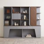 Premium Executive Modern Office Wooden Cabinet in a dual-tone matte grey and walnut woodgrain finish, showcasing a tinted smoked-glass case on the left, open book shelves with a grey ribbed sliding door, a vertical rounded wood panel block on the right next to open side shelving with a pen holder, and lower push-open drawers above a geometric open base cutout, standing on grey textured office carpet tiles.