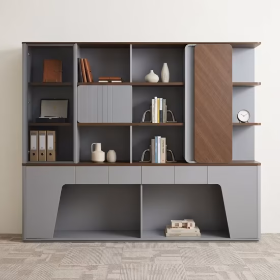 Premium Executive Modern Office Wooden Cabinet in a dual-tone matte grey and walnut woodgrain finish, showcasing a tinted smoked-glass case on the left, open book shelves with a grey ribbed sliding door, a vertical rounded wood panel block on the right next to open side shelving with a pen holder, and lower push-open drawers above a geometric open base cutout, standing on grey textured office carpet tiles.