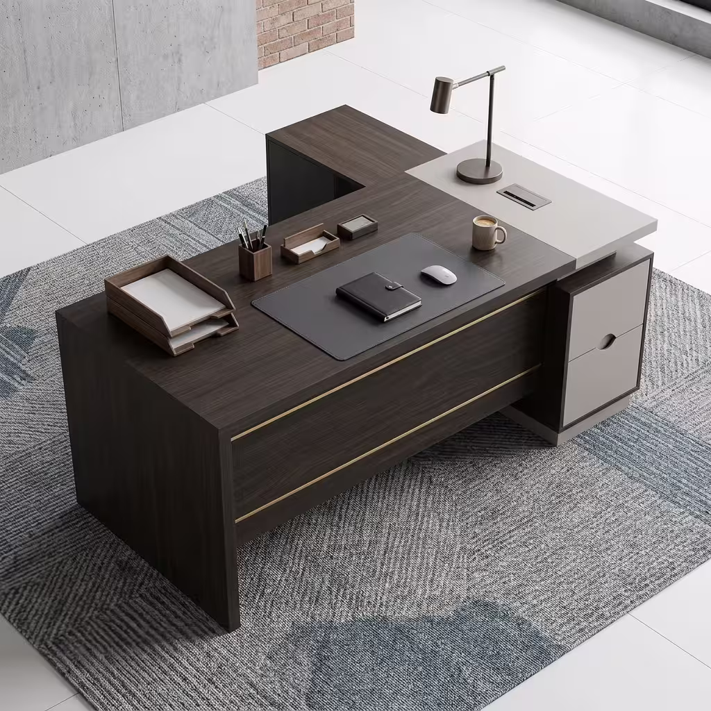 Premium 1.6M L-Shaped Executive Office Desk in a deep charcoal-brown woodgrain finish, featuring a front modesty panel with two horizontal gold accent lines, an integrated stone-grey side return shelf console with an adjustable desk lamp, a flush charcoal leather desk blotter supporting a closed journal and a wireless mouse, and an under-desk storage drawer cabinet, resting on a textured geometric blue-and-grey pattern area rug.
