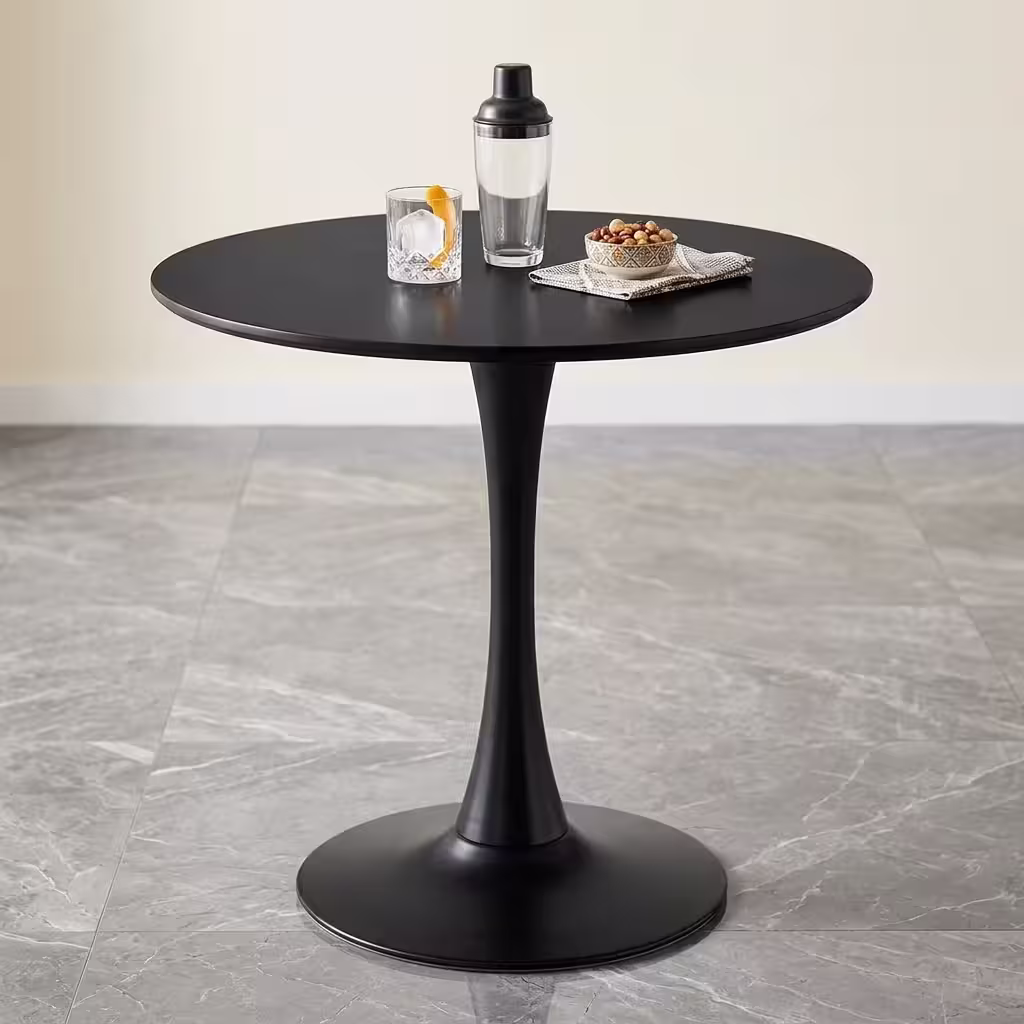 Round Modern Dining Table featuring a sleek black finish, minimalist tulip pedestal base, and a smooth circular top styled with drinks on grey tiles.