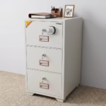Premium 3-Drawer Diplomat Fireproof Office Cabinet in a durable textured white powder-coated steel finish, showing three closed vertically stacked drawers with recessed handles, individual key locks, and a top master electronic digital keypad display panel, standing on light wood flooring in a modern office setup with large wooden bookshelves in the background.