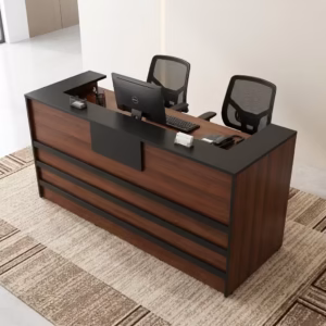 Premium 1.8M Custom Office Reception Desk With Storage in a rich walnut woodgrain and matte black finish, showing an integrated upper privacy counter holding a computer monitor, a desk telephone, and pen organizers, detailed with three horizontal black front accent bands and a central black logo mount board, paired with two black mesh office chairs on a textured beige area rug.