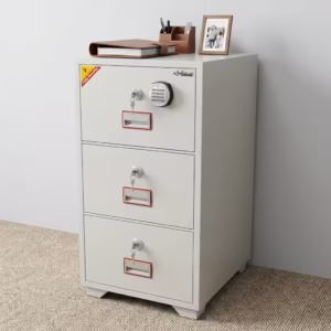 Premium 3-Drawer Diplomat Fireproof Office Cabinet in a durable textured white powder-coated steel finish, showing three closed vertically stacked drawers with recessed handles, individual key locks, and a top master electronic digital keypad display panel, standing on light wood flooring in a modern office setup with large wooden bookshelves in the background.