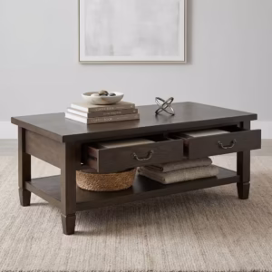 Premium Retro Wooden Coffee Table With Storage in a deep charcoal-brown woodgrain finish, showcasing a rectangular top panel holding stacked books and a ceramic mug on a marble tray, a front section with one closed drawer and one partially open drawer displaying dark metal antique handles, an open lower storage shelf, resting on a thick textured cream area rug in front of a beige fabric sofa.